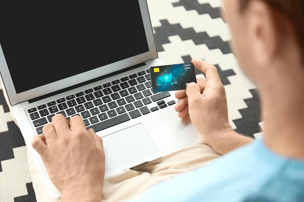 Man holding credit card while using laptop indoors