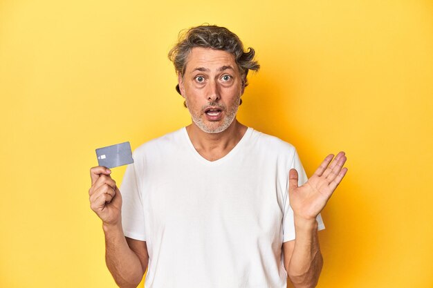 Man holding a credit card yellow studio backdrop surprised and shocked