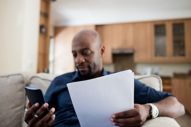 Man holding document while using mobile phone in living room