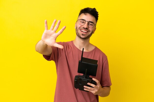 Man holding a drone remote control isolated on yellow background counting five with fingers