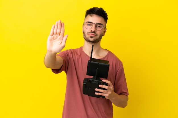 Man holding a drone remote control isolated on yellow background making stop gesture