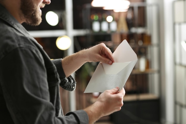 Man holding envelope with greeting card indoors closeup