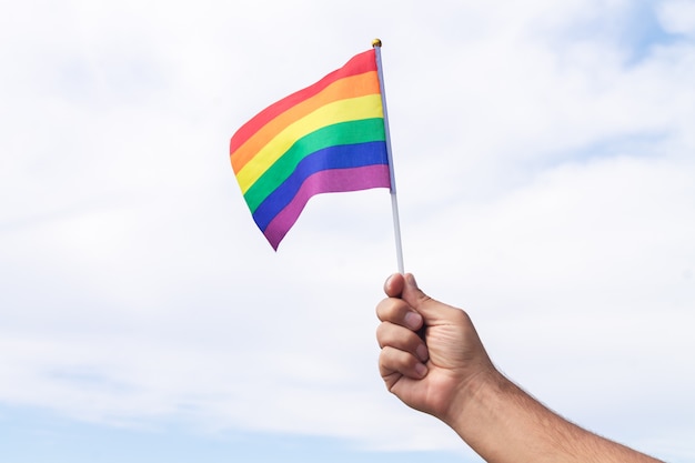 Man holding gay pride symbol rainbow flag on sky background. Same-sex relationships and homosexual concept