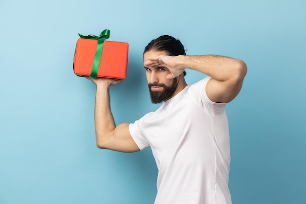 Man holding gift box looks far away with hand over eyes waits future holidays birthday celebration