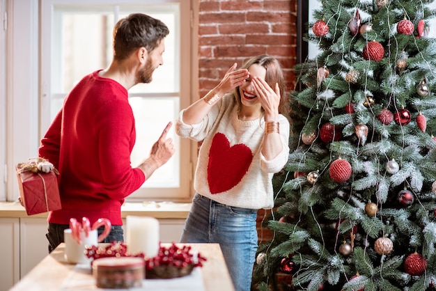 Man holding a gift behind for a young woman celebrating New Year holidays at home