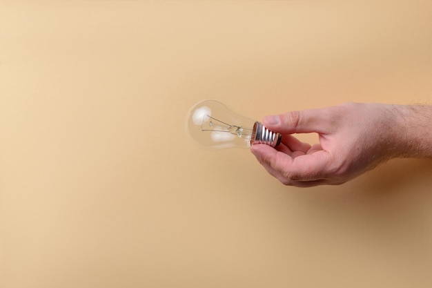 Man holding glass light bulb on beige background with copy space