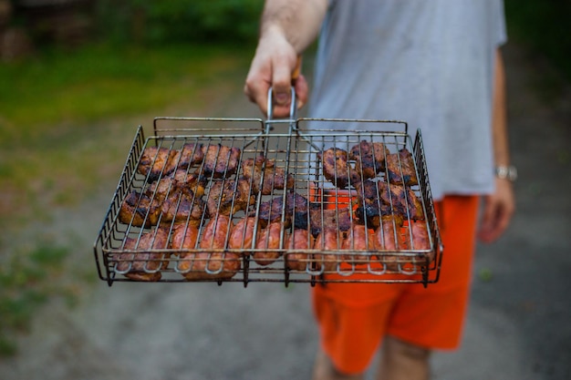 Man holding a grill with meat Rest in the country outside Barbeque Grill Street Food Summer barbecue cooking funny picnic