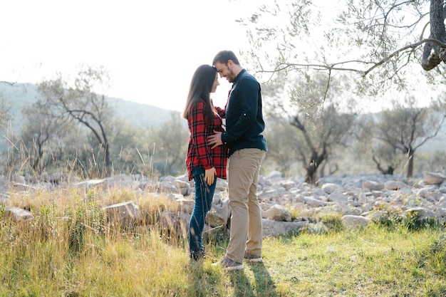 Man holding hands on belly of pregnant woman while standing in park