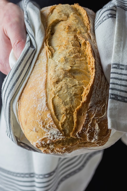 Man Holding in Hands Freshly Baked Hand Crafted Rustic Bread Loaf Wrapped in White cloth.