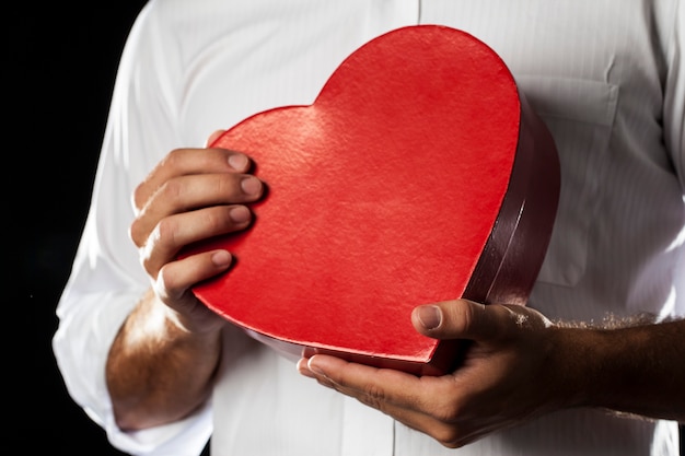 A Man holding a heart gift box in a gesture of giving.