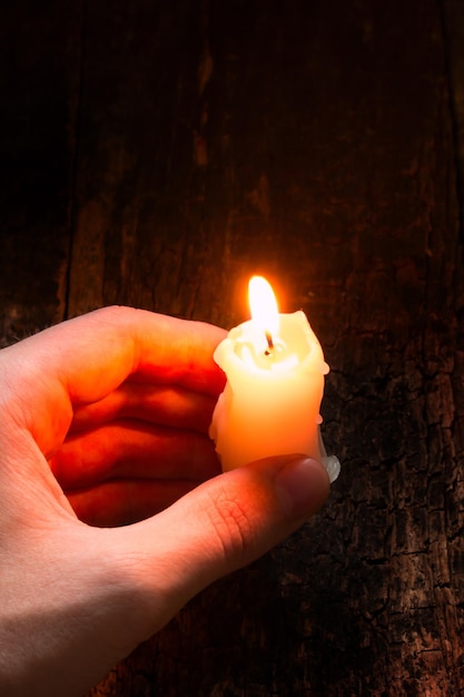 Man holding in his hand a lighted wax candle on a wooden background