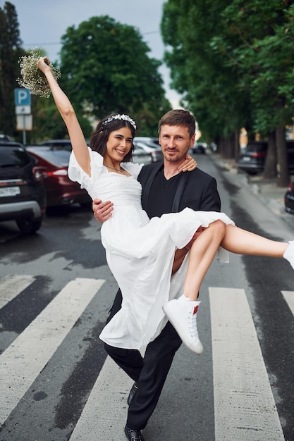 Man holding his woman in hands Beautiful bride with his fiance is celebrating wedding outdoors