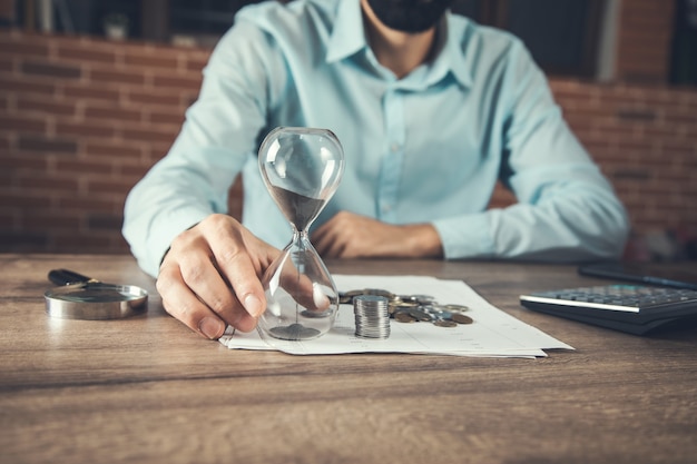 Man holding hourglass and coins stacks on business document