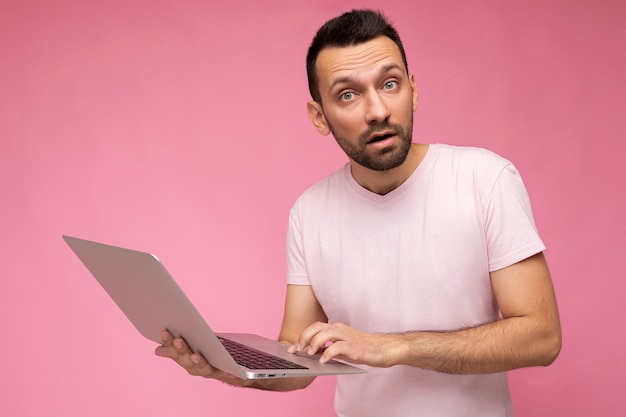 man holding laptop computer looking at camera in tshirt on isolated pink background.