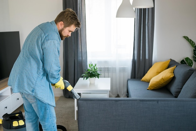 Man holding modern washing vacuum cleaner and cleaning dirty sofa with professionally detergent prof