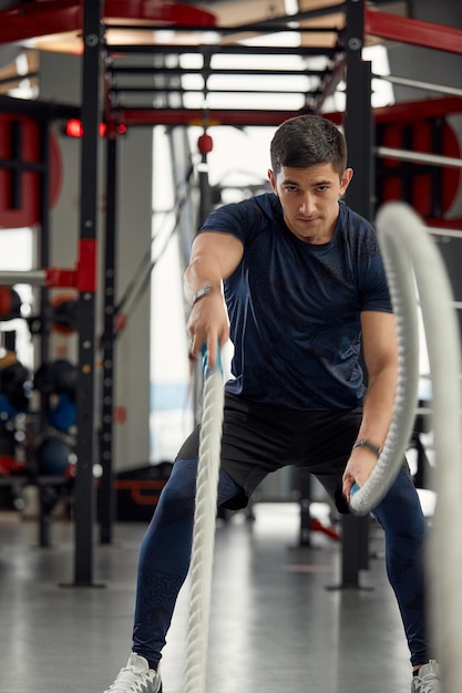 Man holding a pair of battle ropes for workout guy at the gym working out with fitness rope