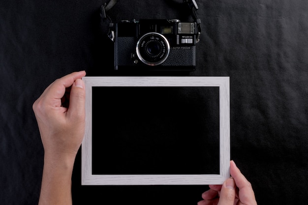 Man holding photo frame and a retro film camera on black background. World photography day.