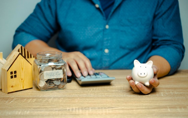 Man holding piggy bank pressing the calculator Calculate income and expenses saving to buy a house