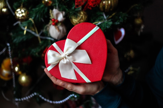 Man holding red heart present box in his hands with  christmas tree decoration