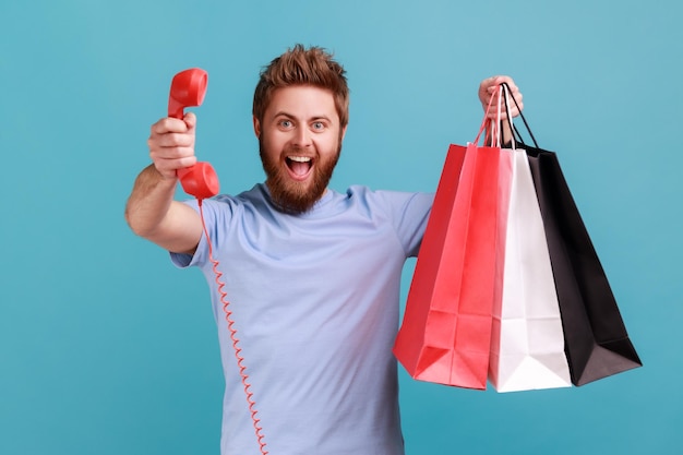 Man holding shopping bag and red retro telephone call me looking at camera with excitement