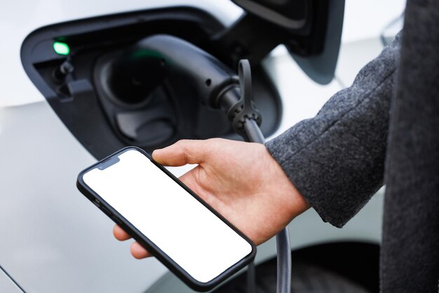 Man holding smartphone while charging car at electric vehicle charging station closeup ev charging