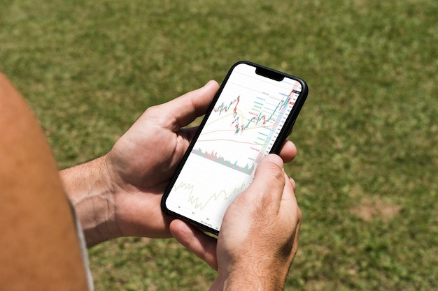 Man holding a smartphone with financial stock market graph on the screen in the park. Stock Exchange.