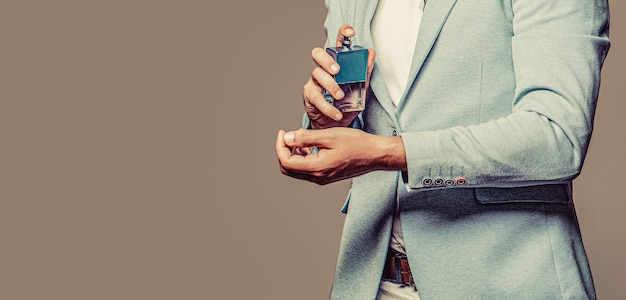 Photo man holding up bottle of perfume men perfume in the hand on suit background handsome man in formal suit and with bottle of perfume closeup