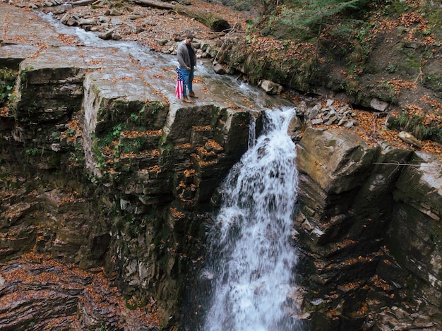 man holding usa flag on the top of the cliff autumn waterfall national park