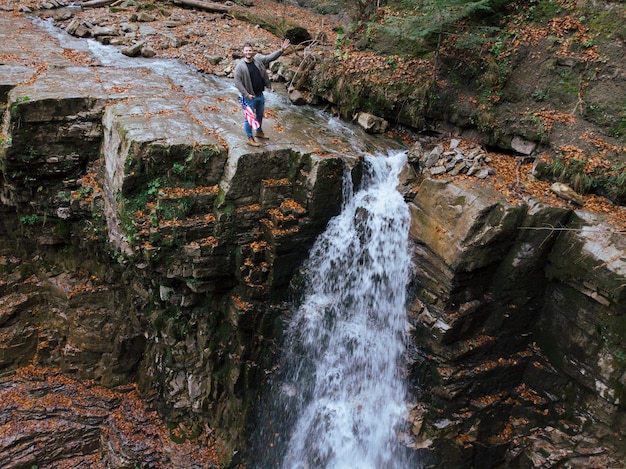 Man holding usa flag on the top of the cliff autumn waterfall