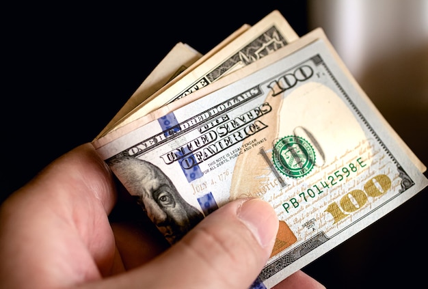 A man holding a wad of US dollar bills in closeup photo with black background