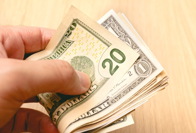 A man holding a wad of US dollar bills in closeup photo with wooden background