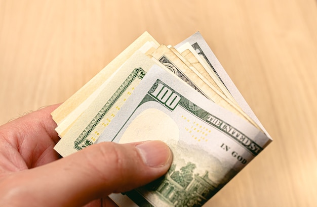 A man holding a wad of US dollar bills in closeup photo with wooden background