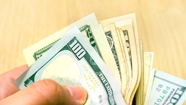 A man holding a wad of US dollar bills in closeup photo with wooden background