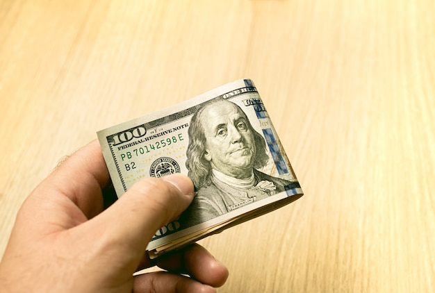 A man holding a wad of US dollar bills in with wooden background