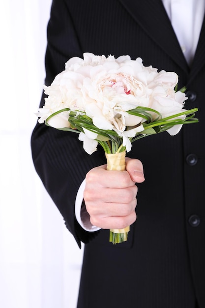 Man holding wedding bouquet on light background