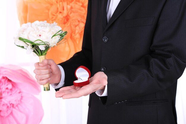 Man holding wedding bouquet and ring on decorative background