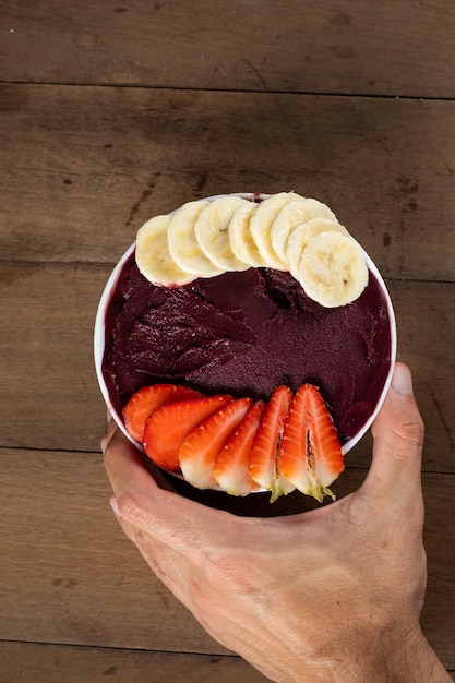 Man holding White Bowl of Brazilian Frozen Acai Berry with Banana and Strawberry on a wooden desk