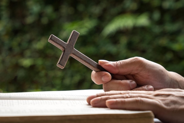 Man holding a wooden religious cross crucifix with an open bible