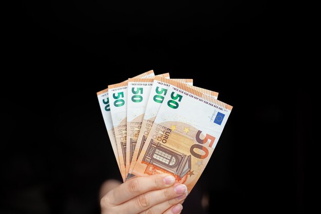 A man holds 100 euro banknotes in his hand on a dark background