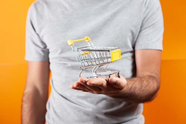 A man holds a cart in his hand. shopping concept on orange background