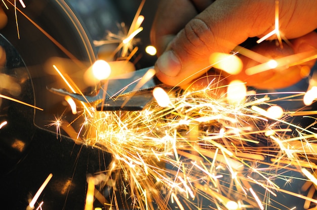 Man holds detail in hand and works with equipment for cutting metal, bright fiery sparks fly apart, closeup photo