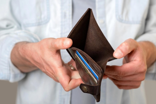 A man holds an empty brown purse with no money Male hands Bankruptcy poverty Isolated gray background