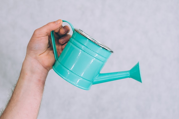 A man holds a garden watering can in his hands on a light.