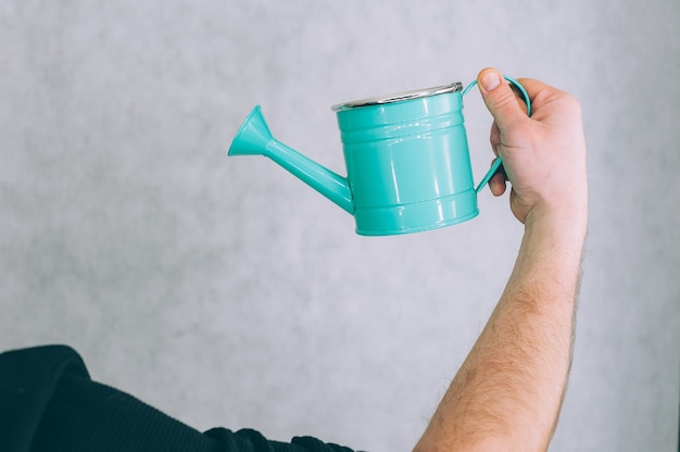 A man holds a garden watering can in his hands on a light.