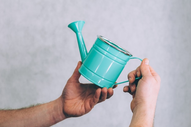 A man holds a garden watering can in his hands on a light.