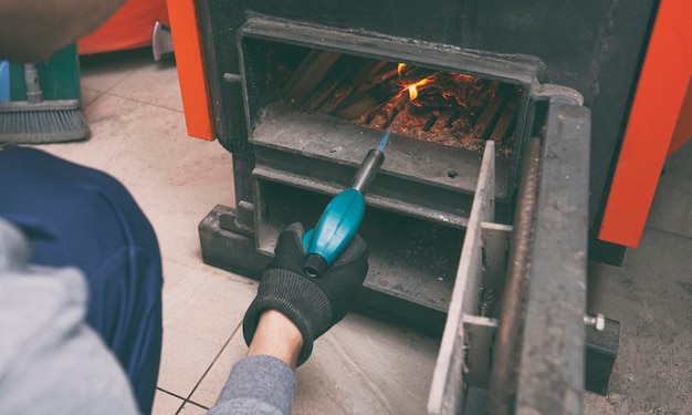 A man holds a gas burner and makes a fire in the solid fuel boiler in the boiler room Solid fuel and heating concept