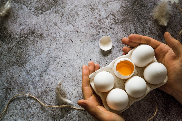 A man holds in his hands fresh farm white chicken eggs on a stand one broken