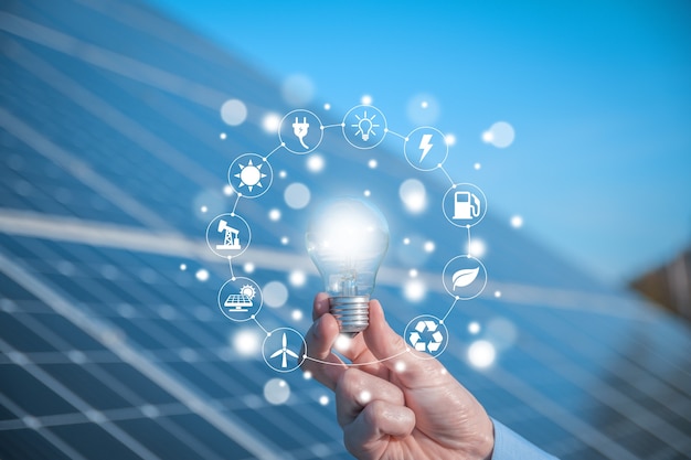 The man holds a light bulb, LED bulb on a background of solar panels with icons energy sources for renewable, sustainable development