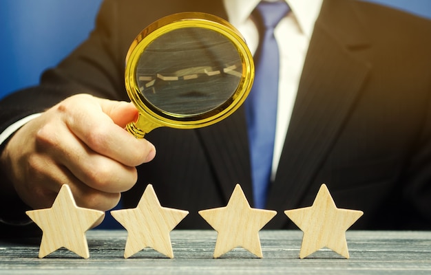 Photo a man holds a magnifying glass over four stars.