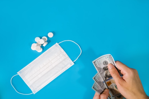 A man holds money in his hand against the background of a medical mask and pill